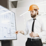 Man in a hard hat pointing at building plans on a screen