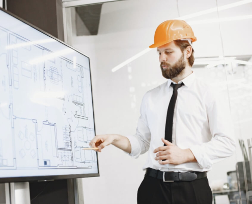 Man in a hard hat pointing at building plans on a screen