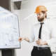 Man in a hard hat pointing at building plans on a screen