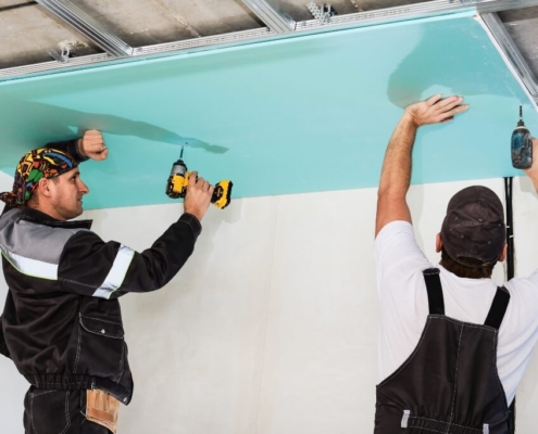 Two men drilling plasterboard into an unfinished ceiling