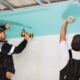 Two men drilling plasterboard into an unfinished ceiling